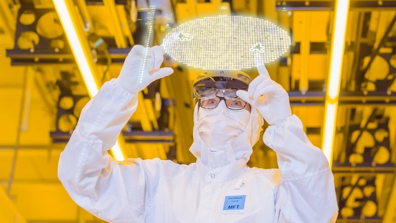 Eine Person in weißer Schutzkleidung blickt auf eine Visualisierung eines Wafers.