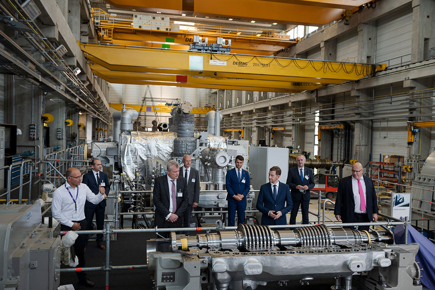 Eine Gruppe von Herren, darunter der sächsiche Ministerpräsident, stehen in einer Halle inmitten von Industriemaschinen.