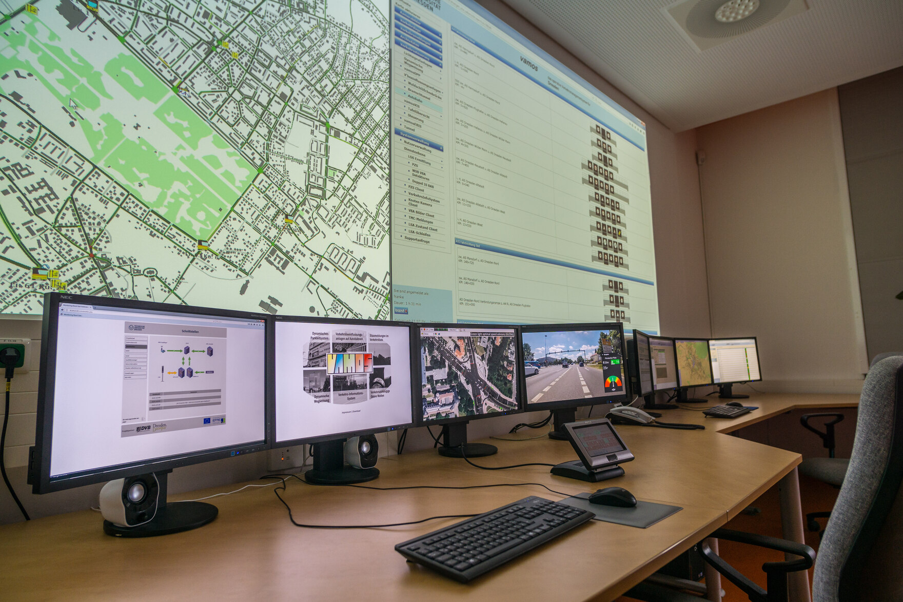Blick in die VAMOS Leitzentrale mit Flachbildschirmen und an eine Wand projezierten Statusmeldungen für das Dresdner ÖPNV Netz