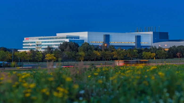 Ein modernes, mehrstöckiges Industriegebäude, umgeben von Bäumen und einer blühenden Wiese