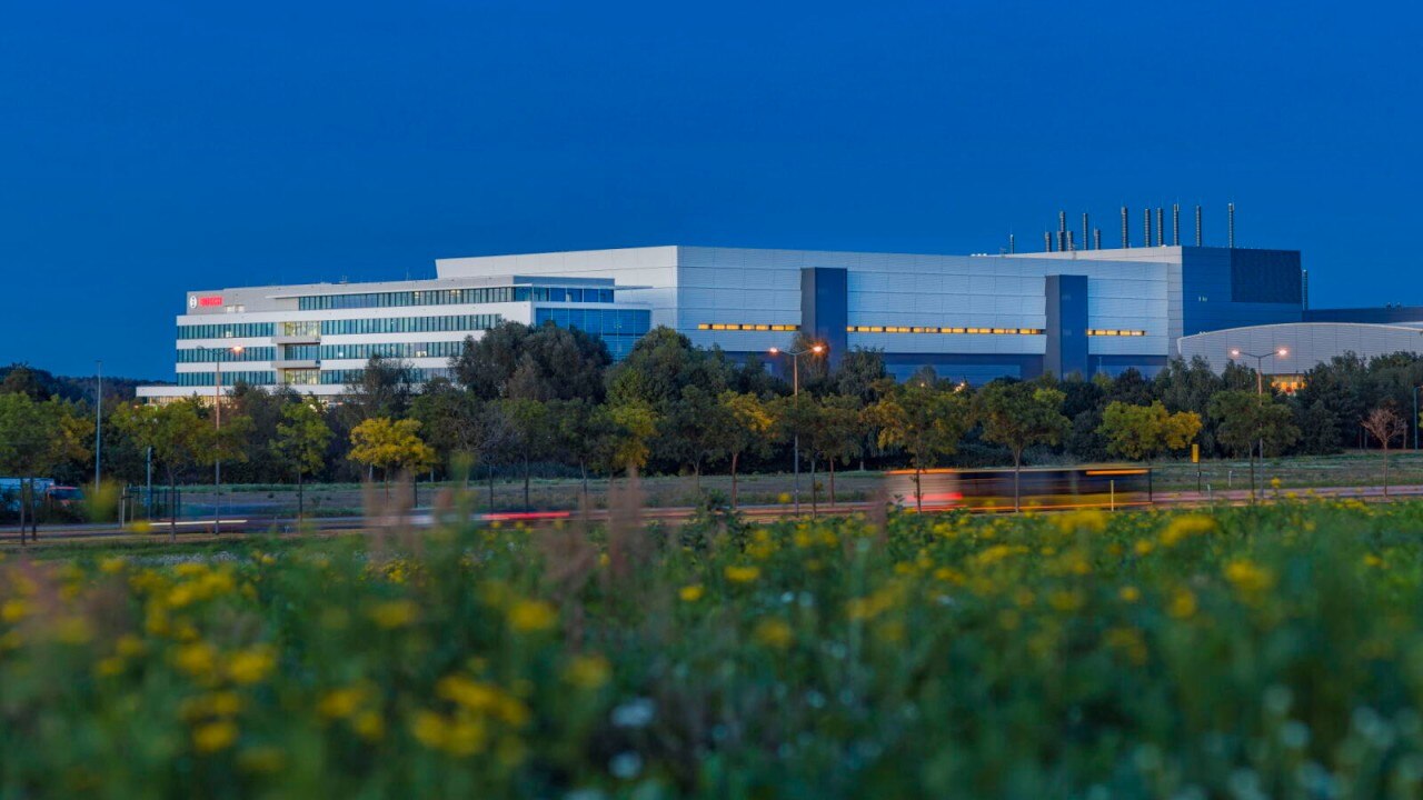 Ein modernes, mehrstöckiges Industriegebäude, umgeben von Bäumen und einer blühenden Wiese