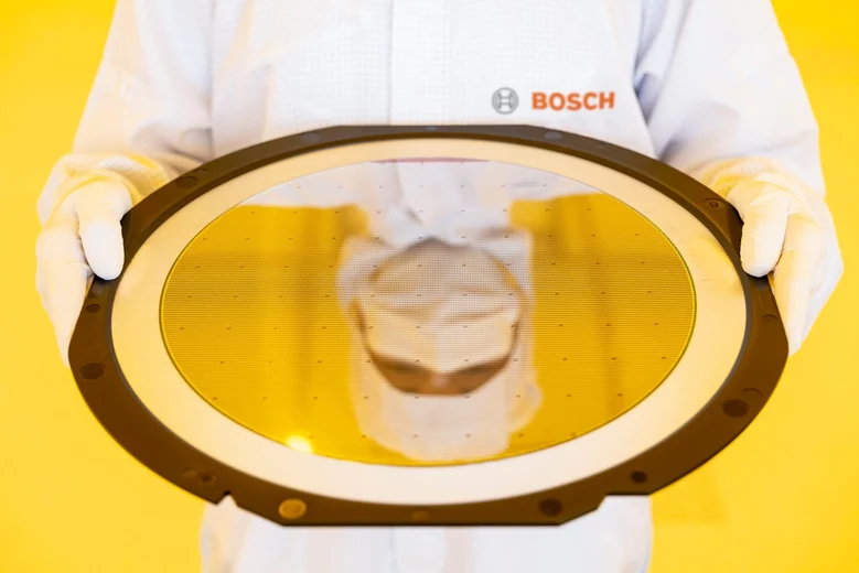 Eine Person in weißer Schutzkleidung spiegelt sich auf einem Wafer.